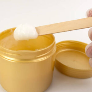 A cosmetic gel from a plastic jar is applied to a wooden spatula.