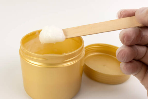 A cosmetic gel from a plastic jar is applied to a wooden spatula.