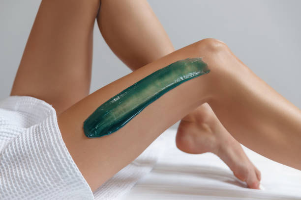 Young woman depilating legs with liquid sugar, wax in spa center.